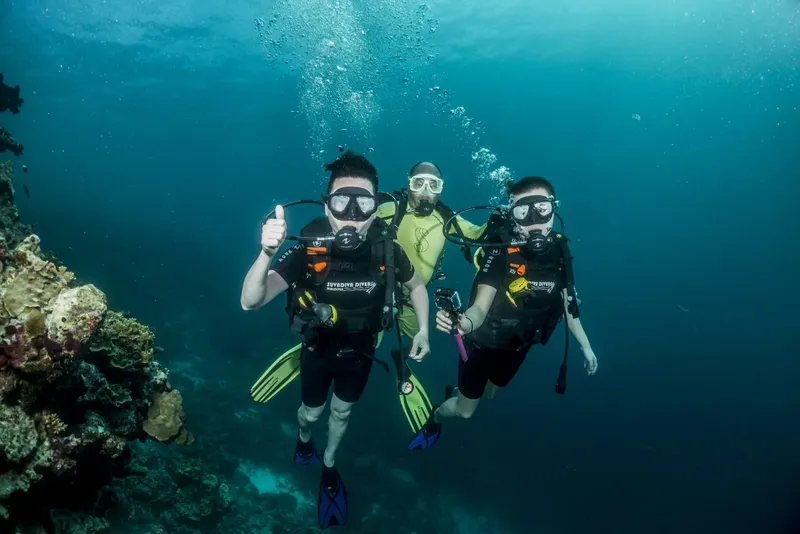 Trois plongeurs souriants évoluent dans une eau bleue et limpide