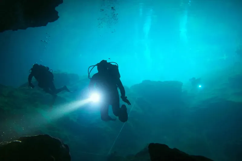 Trois plongeurs explorent un environnement sous-marin bleu et rocheux