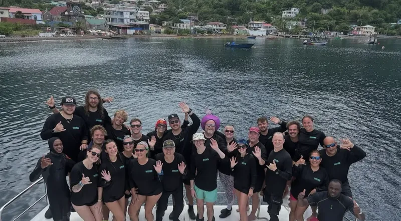 Groupe de plongeurs souriants sur un bateau en mer, paysage côtier