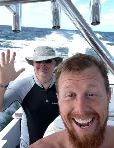 Deux hommes souriants sur un bateau en mer, vagues et soleil