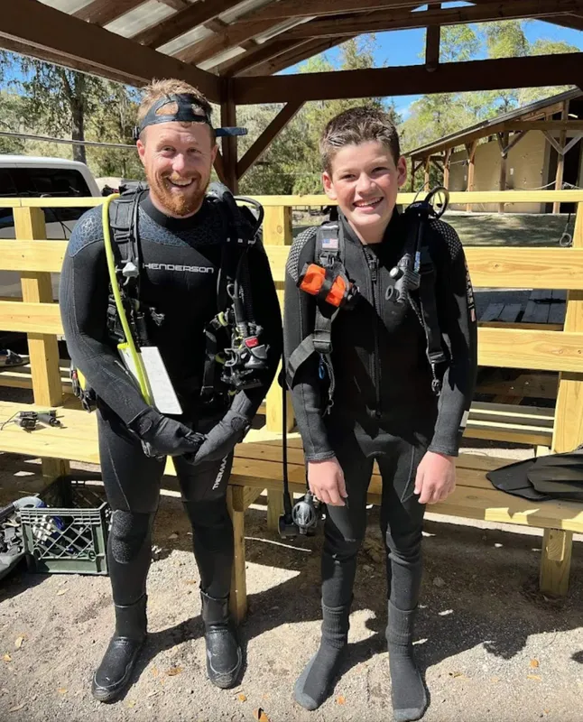Deux plongeurs souriants en combinaison, équipés et prêts à plonger