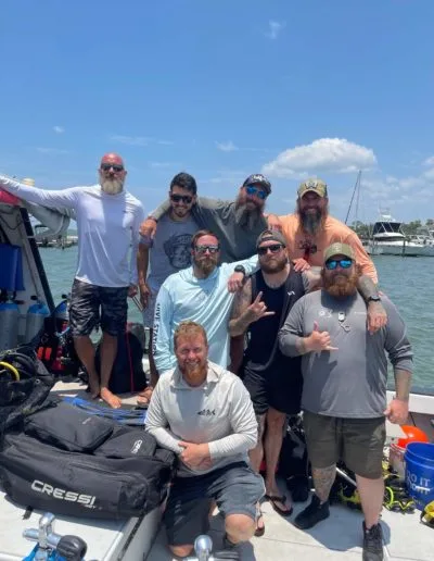 Groupe de plongeurs souriants sur un bateau en mer, équipement visible