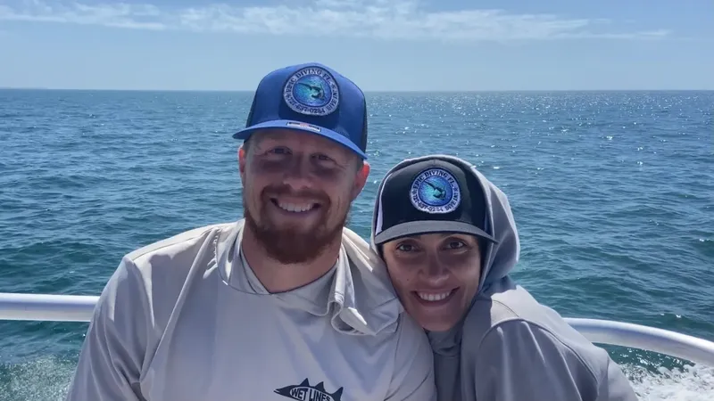Deux personnes souriantes sur un bateau en mer, casquettes aux couleurs vives