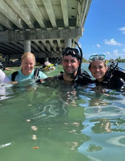 Trois plongeurs souriants avec leur équipement dans une eau claire
