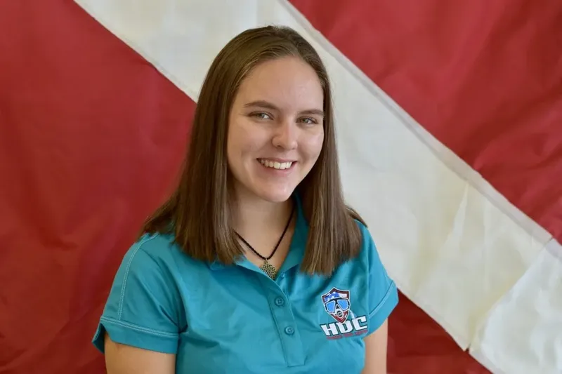 Jeune femme souriante portant un polo bleu devant un fond rouge