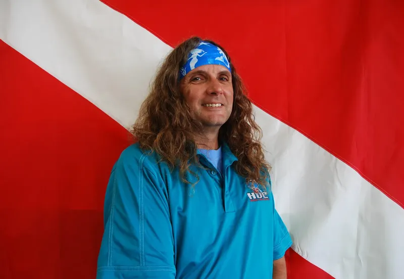 Homme souriant avec bandeau bleu devant un drapeau rouge et blanc