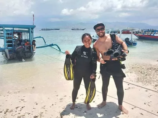 Deux plongeurs souriants sur une plage avec palmes et bouteilles