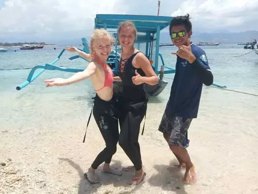 Trois personnes souriantes sur une plage avec des bateaux en arrière-plan
