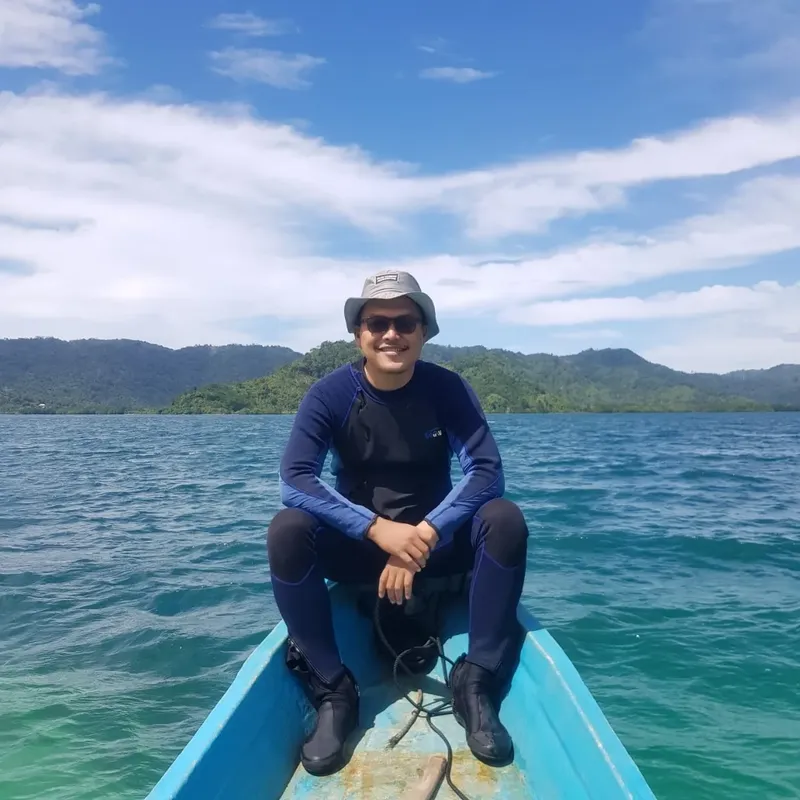 Plongeur souriant assis dans une barque sur mer turquoise