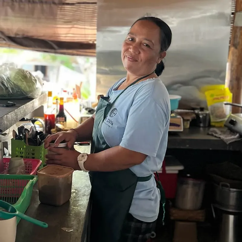 Femme souriante dans une cuisine, portant un tablier et une chemise