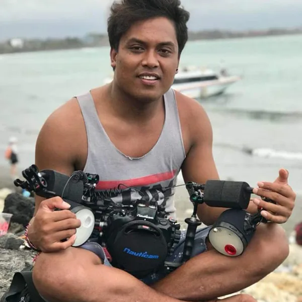Un homme souriant tient un appareil photo sous-marin sur une plage