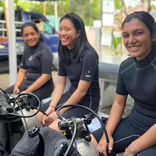 Trois plongeuses souriantes assises avec leur équipement de plongée