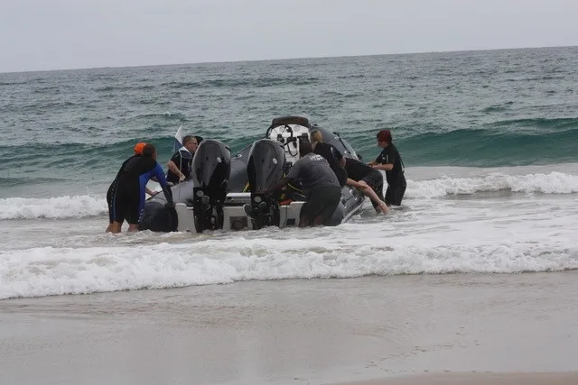 Groupe de personnes sort un bateau semi-rigide de l'eau sur une plage