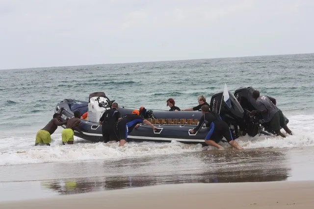 Plongeurs aident à sortir un bateau semi-rigide de l'eau sur une plage