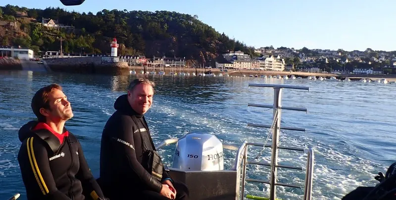 Deux plongeurs en combinaison sur un bateau en mer, paysage côtier