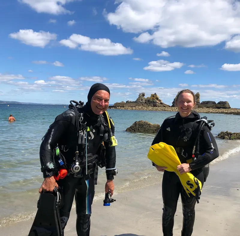 Deux plongeurs souriants équipés sur une plage ensoleillée