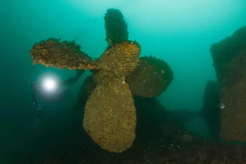 Hélice rouillée d'épave sous-marine, un plongeur avec lampe éclaire