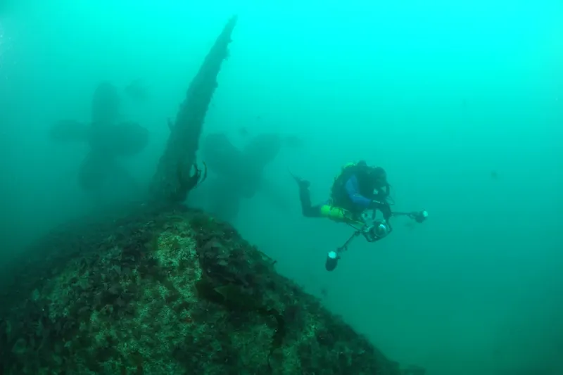 Plongeur explorant une épave sous-marine dans une eau turquoise
