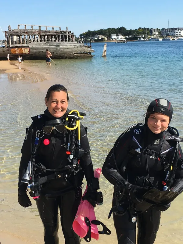 Deux plongeuses souriantes en combinaison sur une plage ensoleillée
