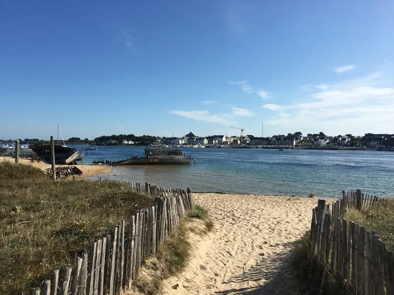 Plage de sable, bateaux amarrés, vue sur un port et un ciel bleu