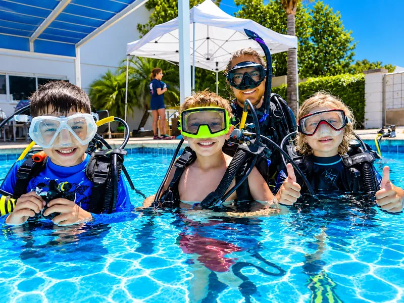 Quatre personnes souriantes en équipement de plongée dans une piscine