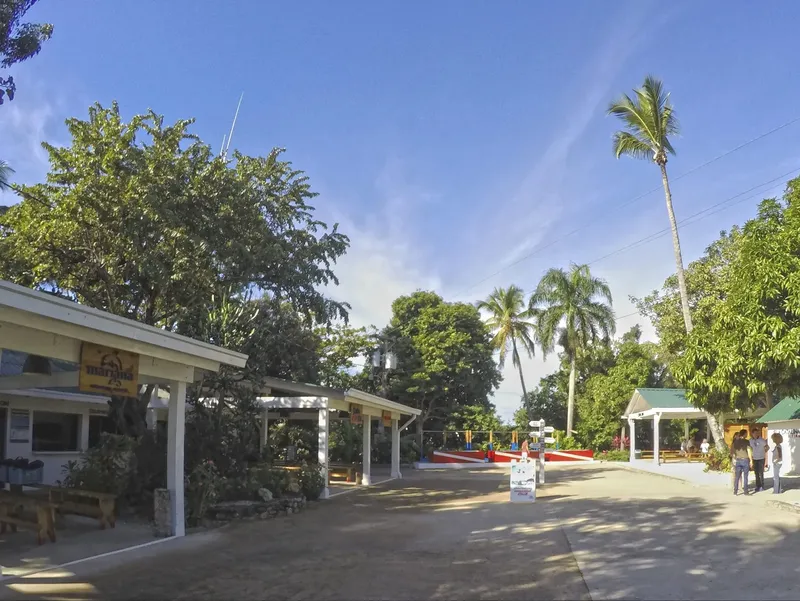 Bâtiments blancs, végétation tropicale, personnes se promènent sur un parking ensoleillé