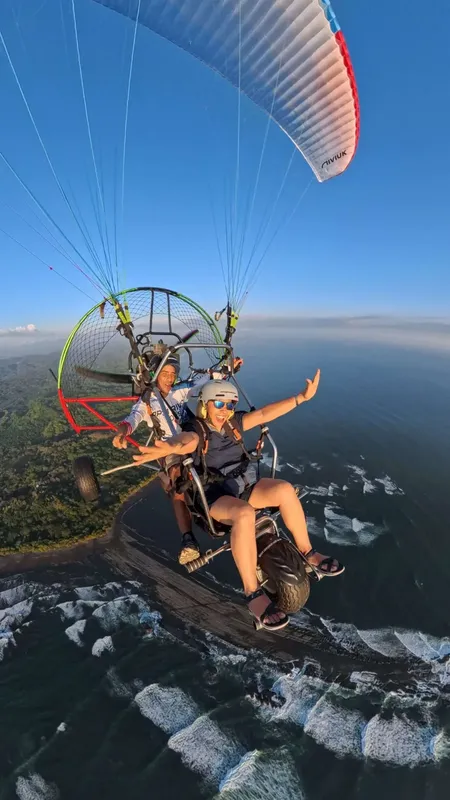 Deux personnes en parapente motorisé survolent un paysage côtier