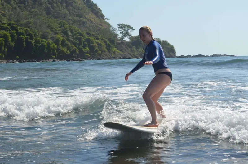 Une surfeuse sur une vague, paysage côtier ensoleillé et végétation luxuriante