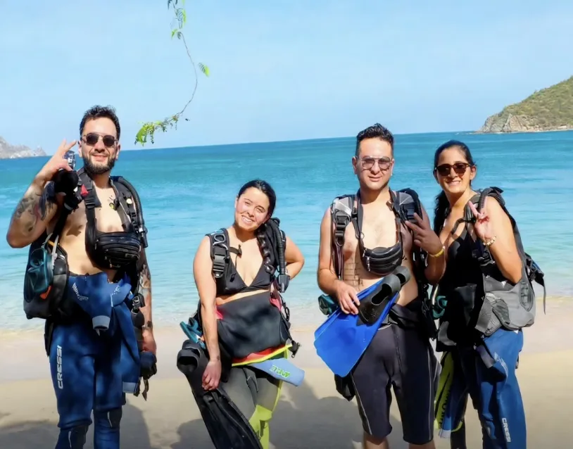Quatre plongeurs souriants posent sur une plage avec leur équipement