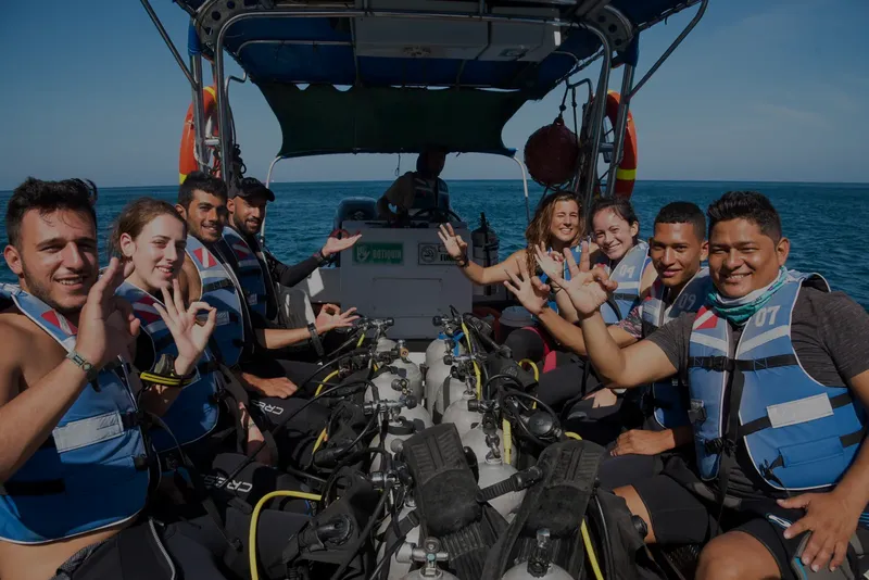 Groupe de plongeurs souriants sur un bateau, équipés et prêts à plonger