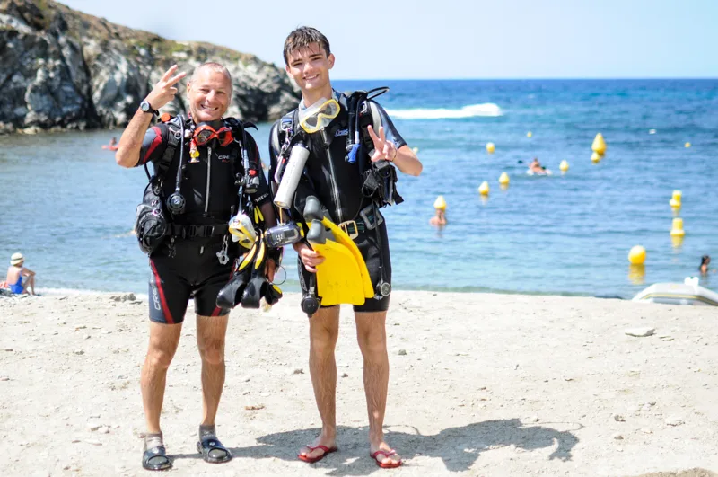 Deux plongeurs souriants font un signe de la main sur une plage