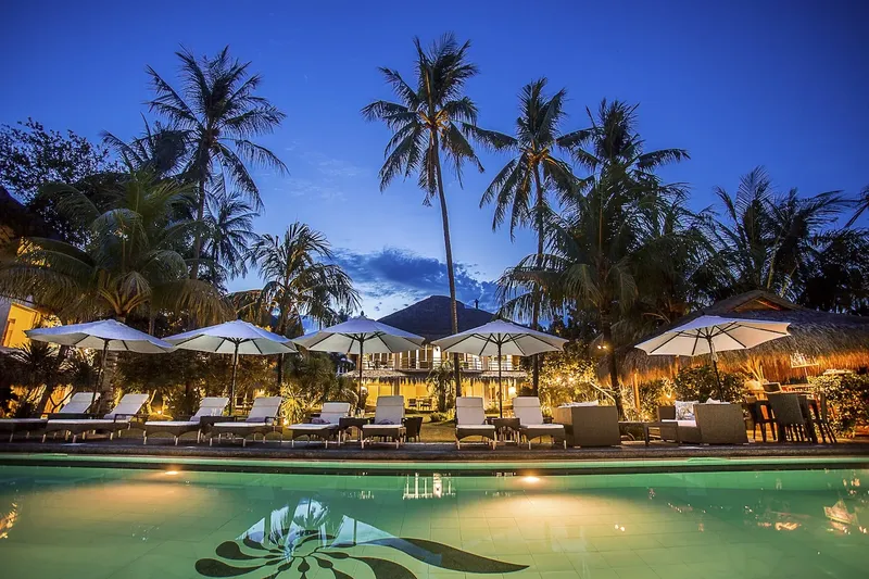 Piscine éclairée avec transats et bâtiments tropicaux au crépuscule