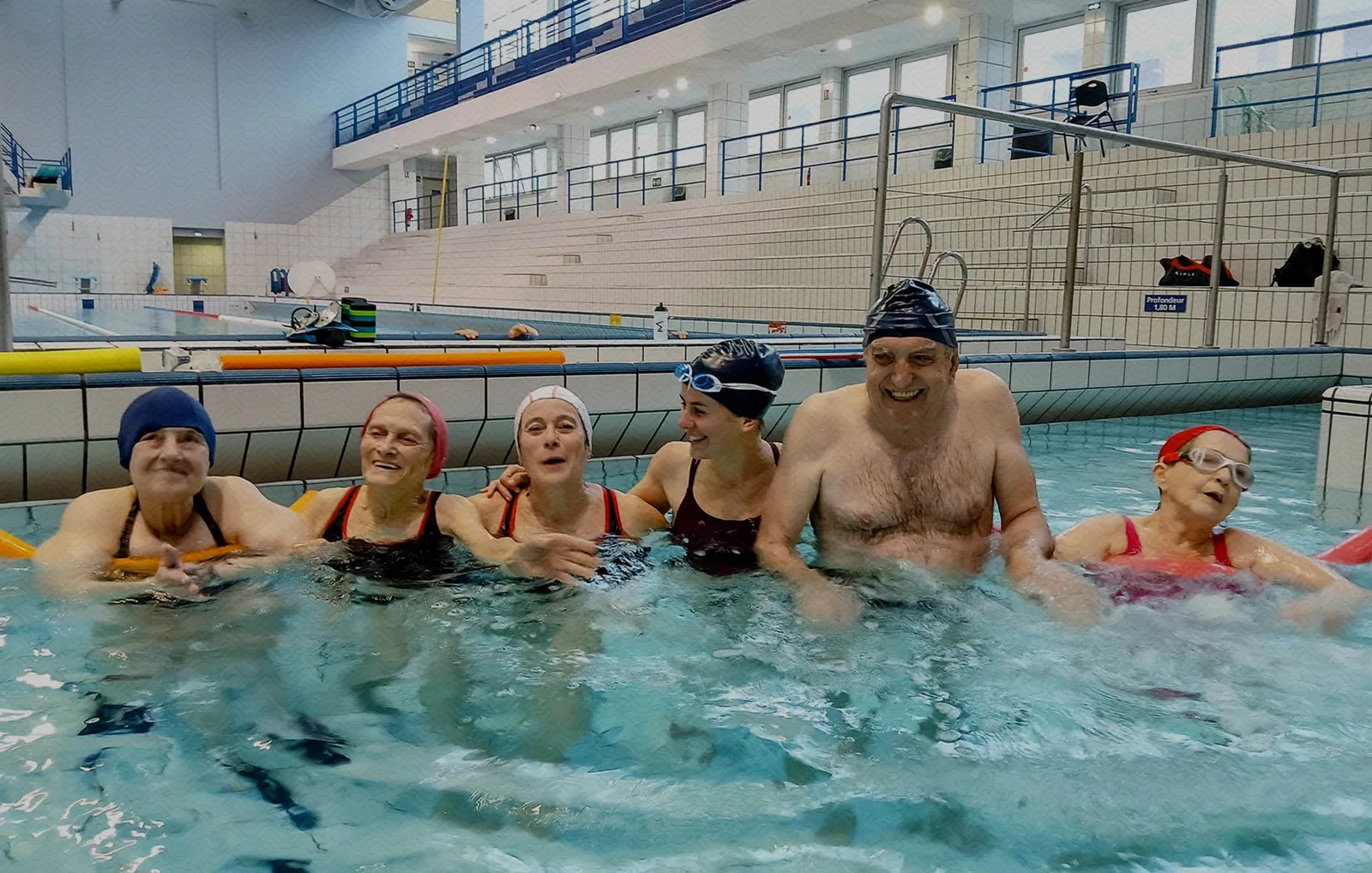 Groupe de personnes souriantes dans une piscine intérieure, cours de natation