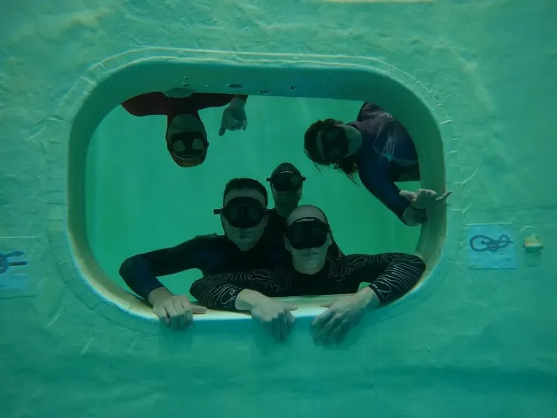 Quatre plongeurs souriants regardent à travers une ouverture sous-marine