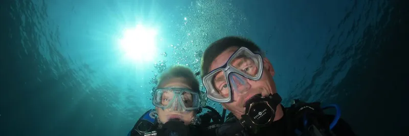 Deux plongeurs sourient à la caméra, bulles et lumière du soleil