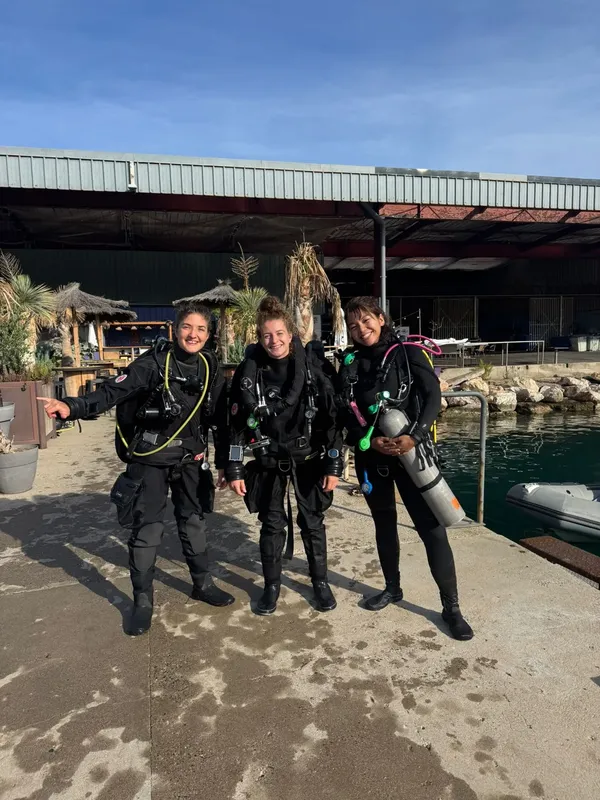 Trois plongeuses souriantes équipées près d'un ponton ensoleillé