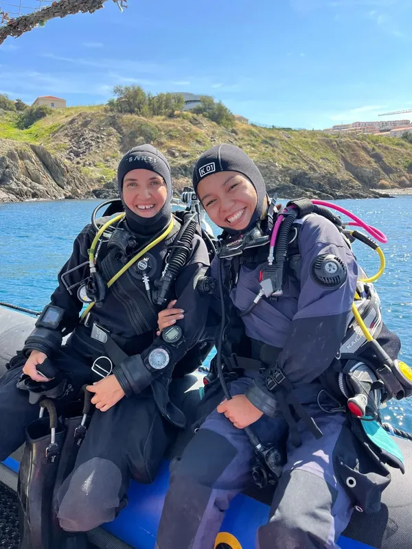 Deux plongeuses souriantes en combinaison sur un bateau pneumatique bleu