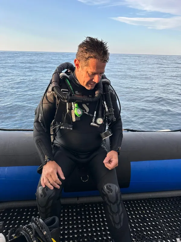 Plongeur en combinaison assis sur un bateau, préparant son équipement