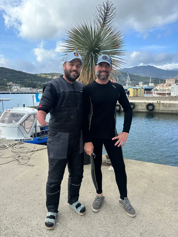 Deux hommes souriants en tenue de plongée près d'un bateau et d'un quai