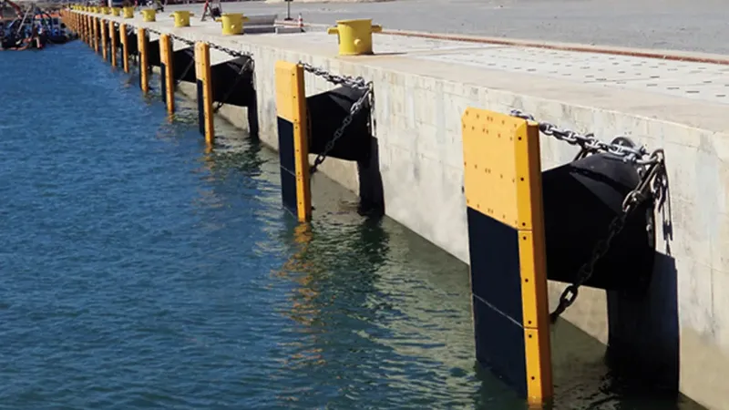 Quai de béton avec défenses noires et jaunes, chaînes métalliques, eau