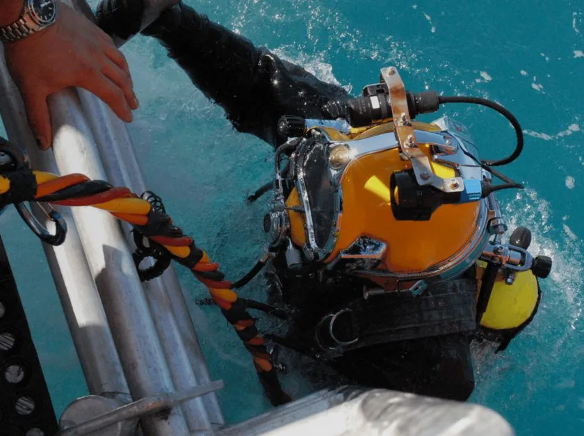Plongeur avec casque lourd descendant d'un bateau en mer