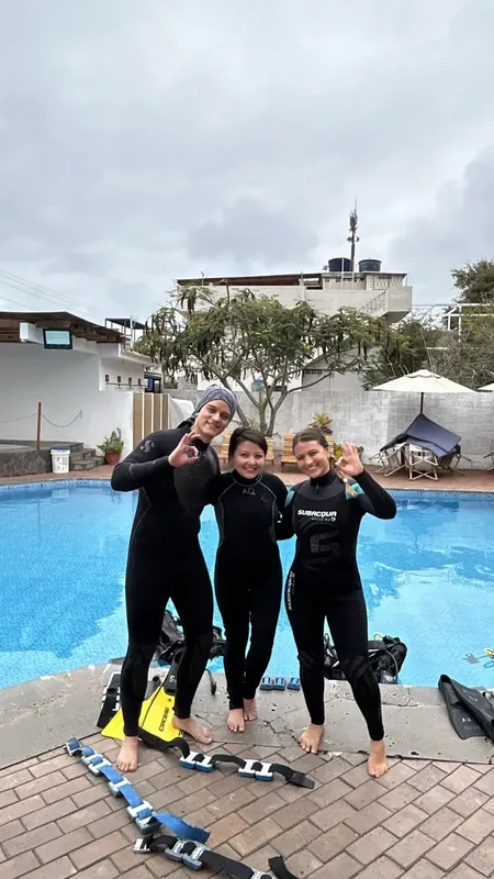 Trois plongeuses souriantes en combinaison près d'une piscine et du matériel