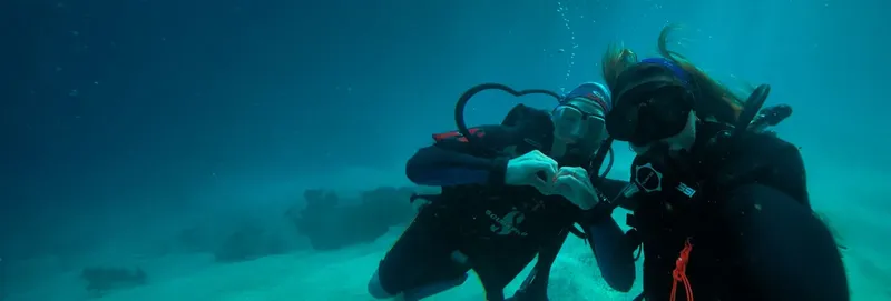 Deux plongeurs en combinaison, équipés, communiquent sous l'eau dans un environnement bleu