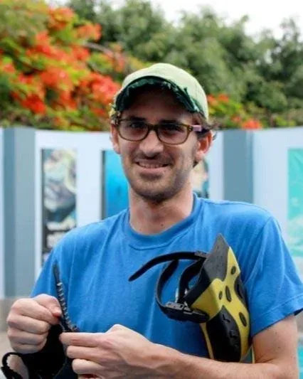 Plongeur souriant tenant palmes et masque devant un mur coloré