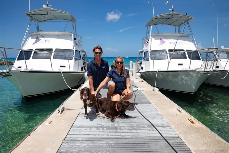 Couple et chiens sur un ponton devant des bateaux de plongée