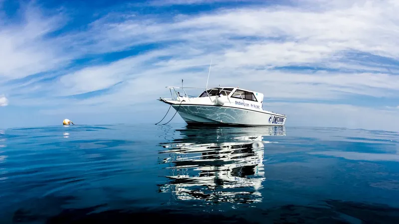 Bateau de plongée blanc sur mer calme avec reflet et ciel nuageux