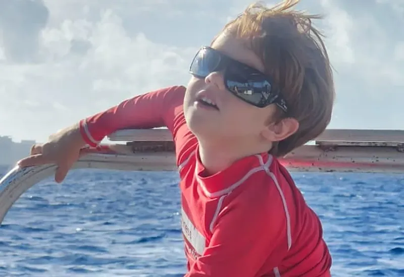 Jeune enfant souriant avec des lunettes de soleil sur un bateau