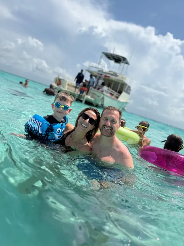 Famille souriante dans l'eau turquoise avec un bateau en arrière-plan