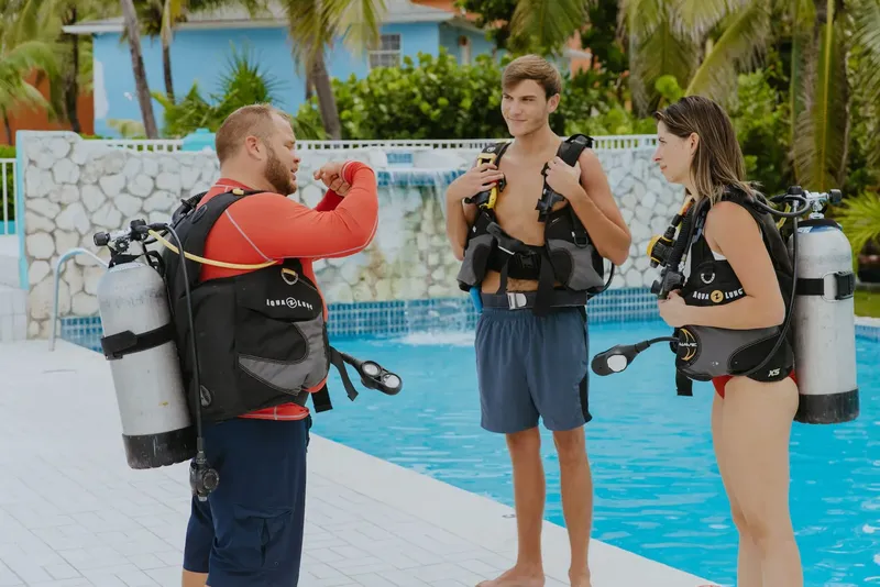 Trois personnes équipées pour la plongée discutent près d'une piscine