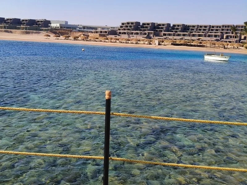 Vue sur une plage avec un bateau, l'eau turquoise et des parasols